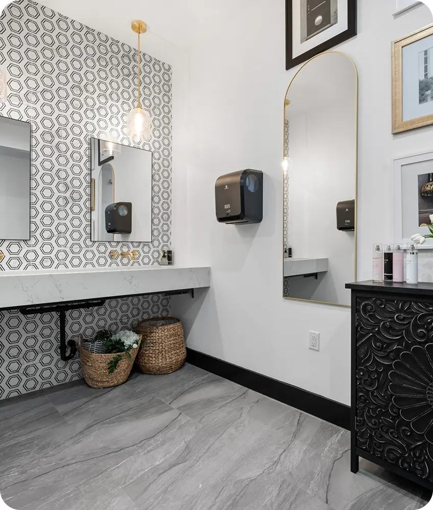 A chic vanity area with a marble floating counter, hexagonal tile backsplash, gold accents, and a large arched mirror.